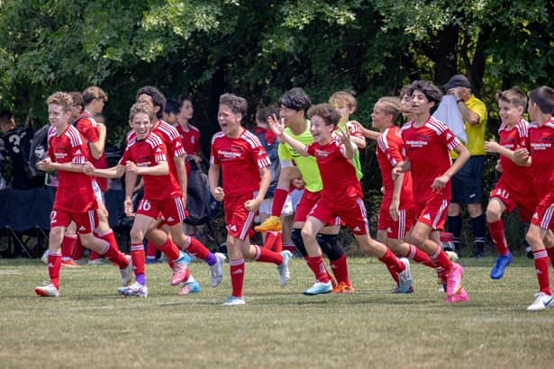 A group of teenage boys in red Parkland Area Soccer Club jerseys running and cheering excitedly across a grass field.